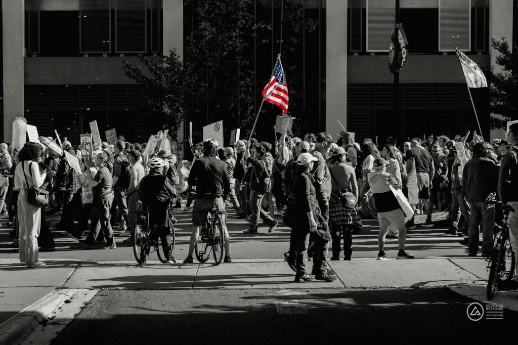 Crowd of protesters holding signs and American flags at a demonstration in the city.