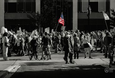 Crowd of protesters holding signs and American flags at a demonstration in the city.