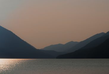 Calm mountain lake with sunset reflections and surrounding peaks.